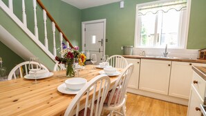 A dining area with a wooden table set for four, white chairs, and a vase of flowers. - 1 Foresters Rest (Alton)