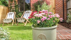 A potted plant with pink flowers in front of a brick house with two wooden chairs. - 1 Foresters Rest (Alton)