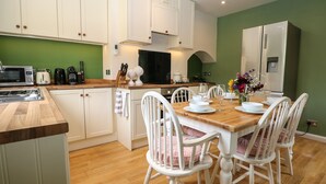 A modern kitchen with white cabinetry, a wooden countertop, and a dining area with white chairs and a wooden table set for four. - 1 Foresters Rest (Alton)