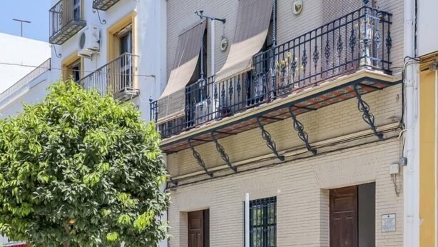 A multi-story building with balconies, a tree in front, and a sign indicating a business on the ground floor. - Enjoy the magic of Triana Sevilla, Calle Castilla (Sevilla)