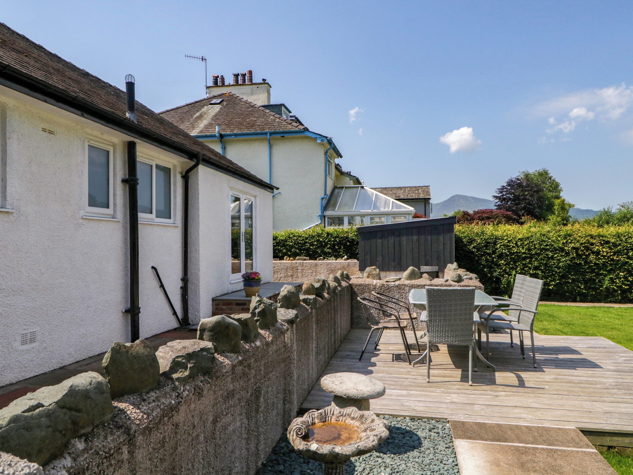 A house with a stone wall, a wooden deck, outdoor furniture, and a garden.