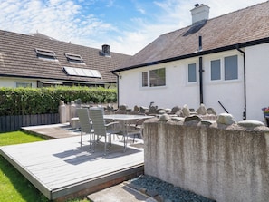 Un patio con tavolo e sedie, un muro in pietra e una casa con tetto in tegole e finestre.