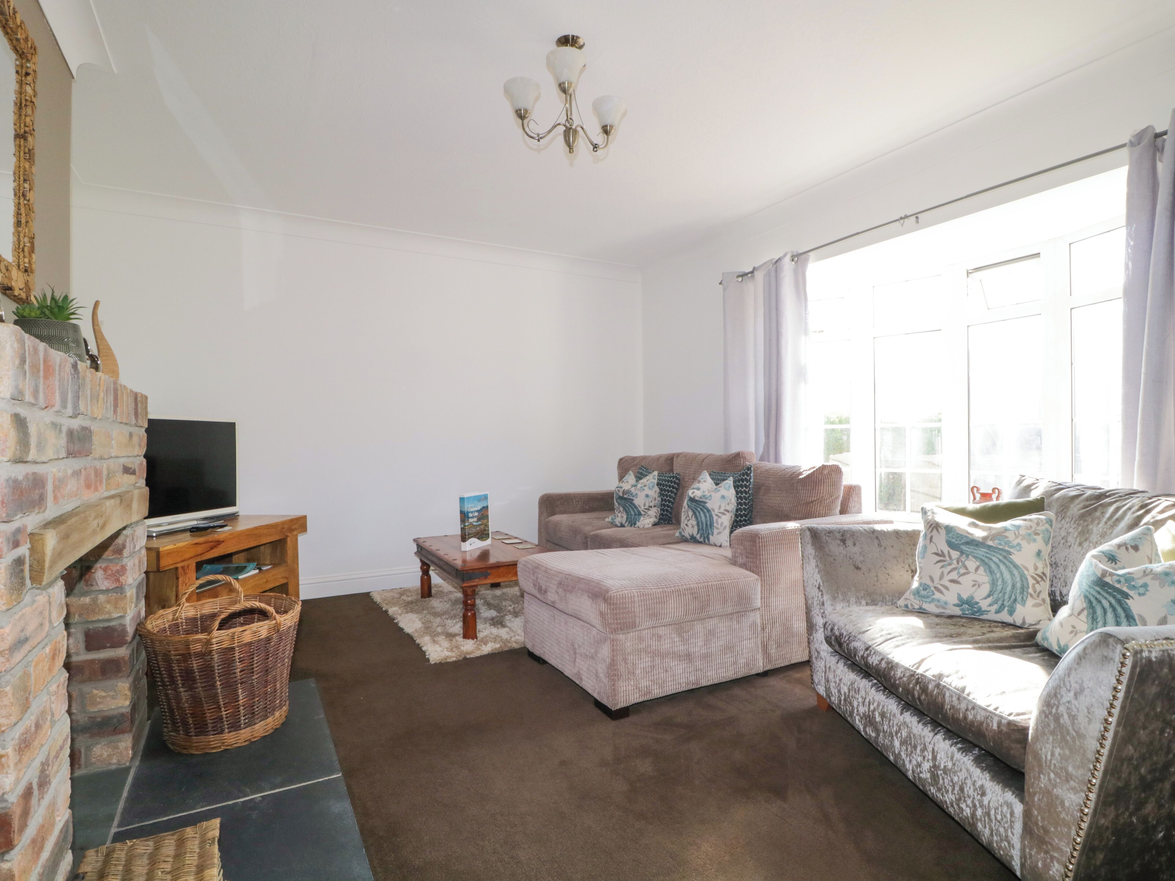 A living room with a brick fireplace, a television, a sofa, and a window with curtains.