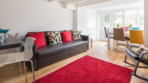 Ein modernes Wohnzimmer mit einem schwarzen Ledersofa, einem roten Teppich und einem Essbereich inklusive Tisch und Stühlen.