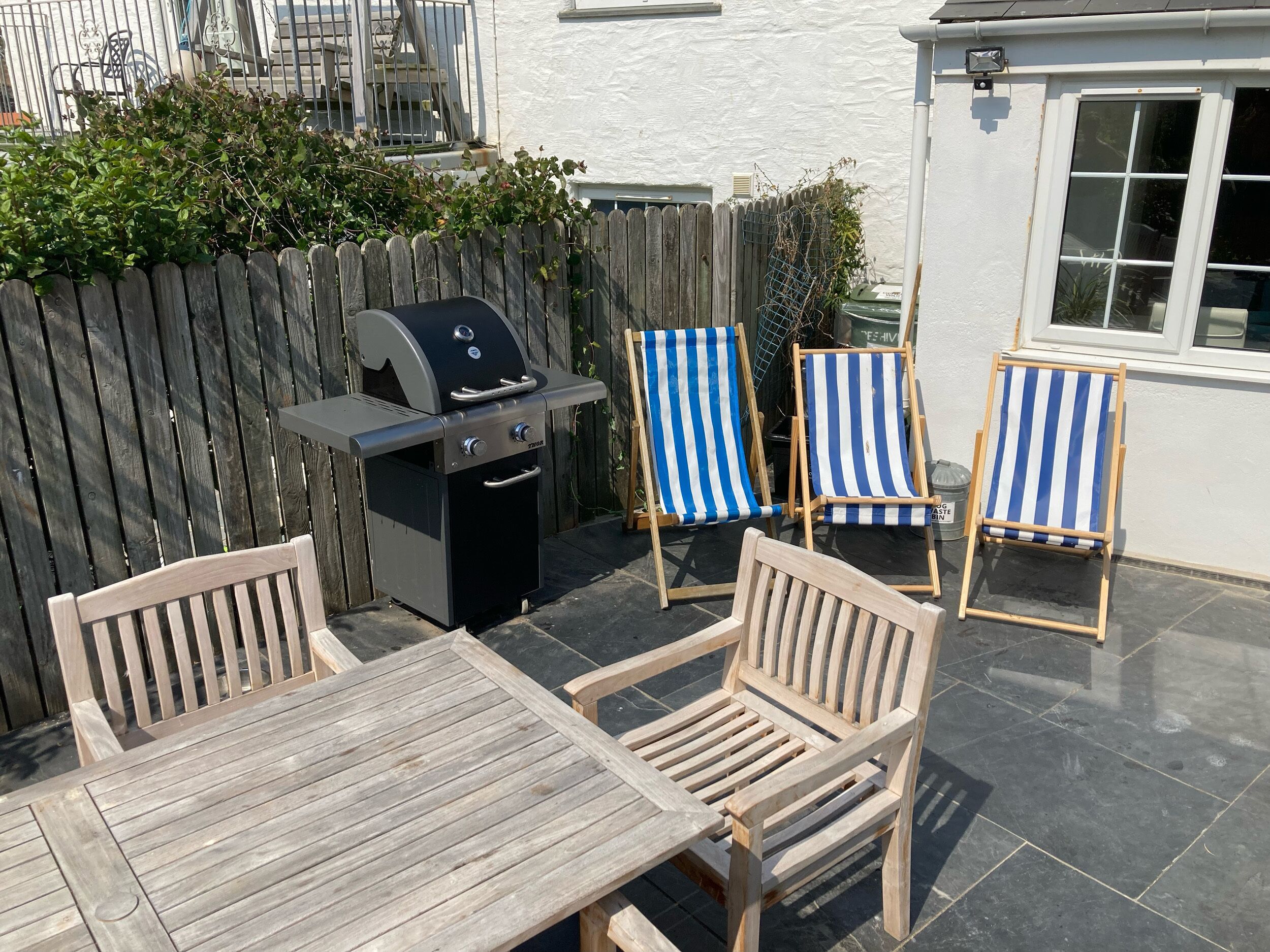 A patio with a grill, two striped beach chairs, and a wooden table.