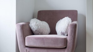 Ein rosa Sessel mit Holzbeinen und zwei flauschigen wei ßen Kissen.