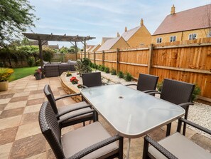 Un patio al aire libre con una mesa, sillas, una pérgola y una valla de madera.