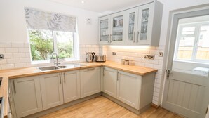 Una cocina moderna con armarios de colores claros, encimera de madera y una ventana con persiana estampada con motivos de hojas.