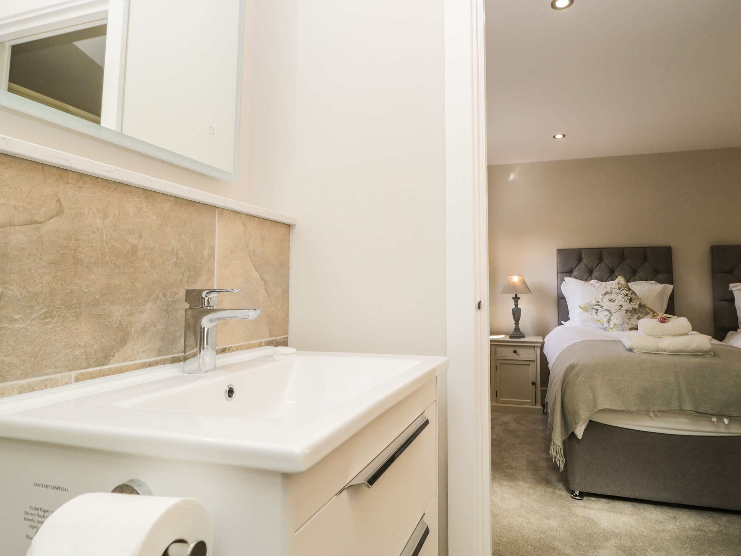Une salle de bain d’hôtel équipée d’un lavabo, d’un miroir et d’un distributeur de papier toilette.