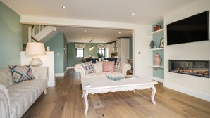 A spacious living room with a white sofa, a coffee table, and a fireplace. - Tarn End Cottages 12 (Brampton)