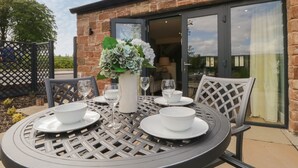 An outdoor dining area with a round table, chairs, and a vase of flowers. - Tarn End Cottages 12 (Brampton)