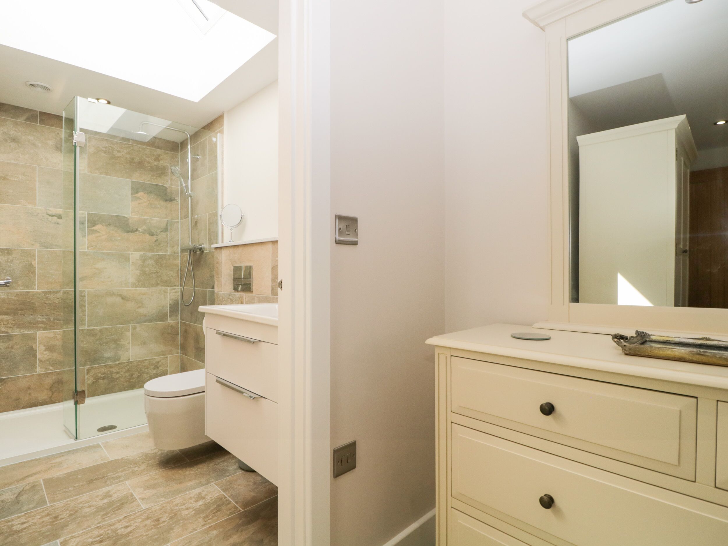 Un baño moderno con cabina de ducha de vidrio, inodoro y tocador con cajones.