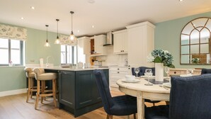 A kitchen with a central island, bar stools, and a dining table with chairs. - Tarn End Cottages 12 (Brampton)