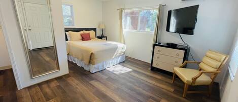 A bedroom with a bed, a dresser, a chair, a TV, and an air conditioning unit.