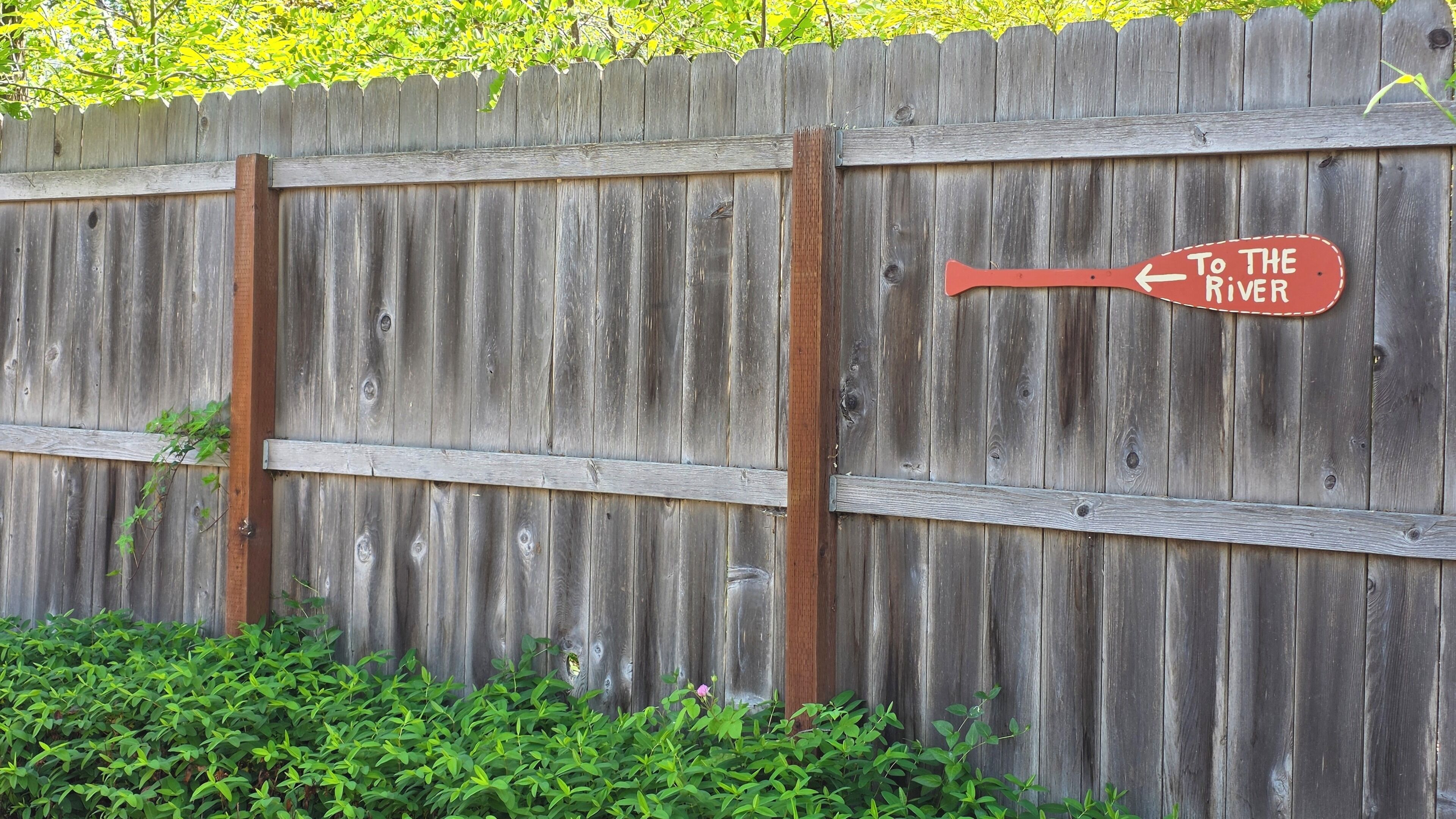 A wooden fence with a directional sign pointing to the river.