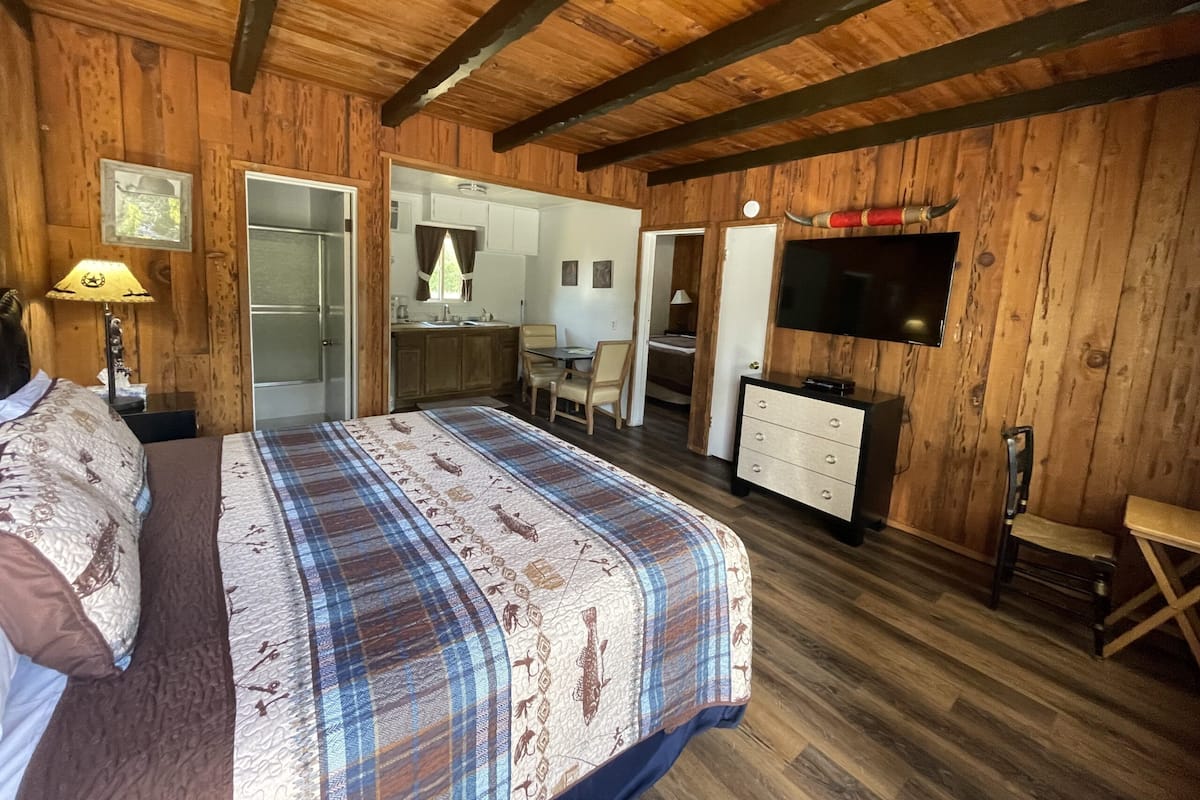 A wooden-paneled bedroom with a bed, a dresser, a television, and a bathroom visible through an open door.