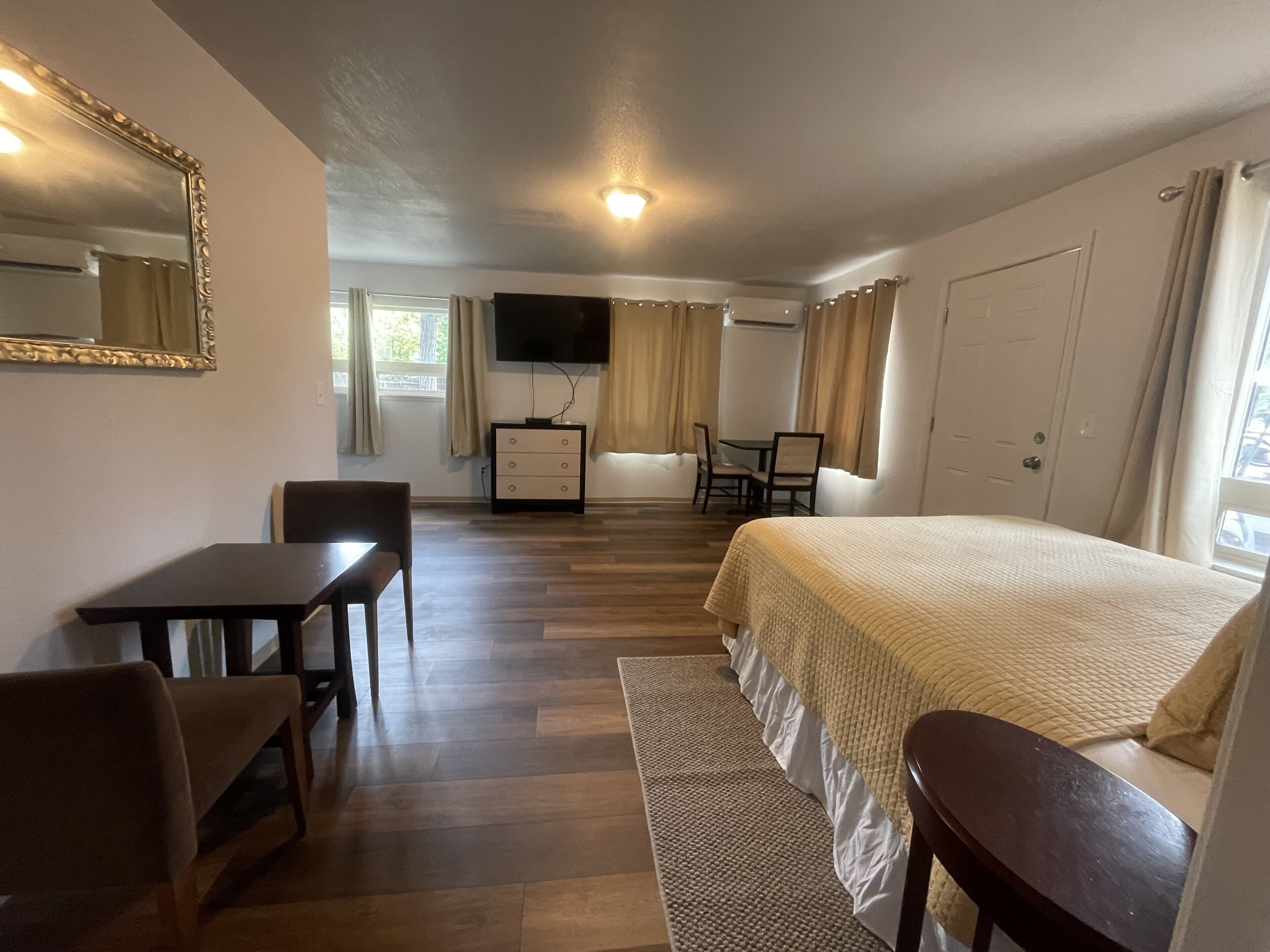 Una camera d'albergo con un letto, una scrivania, una sedia, una TV e una finestra con tende.