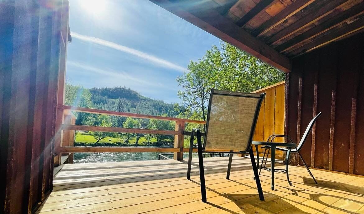 A wooden deck with a view of a river and forest, a chair, and a table.