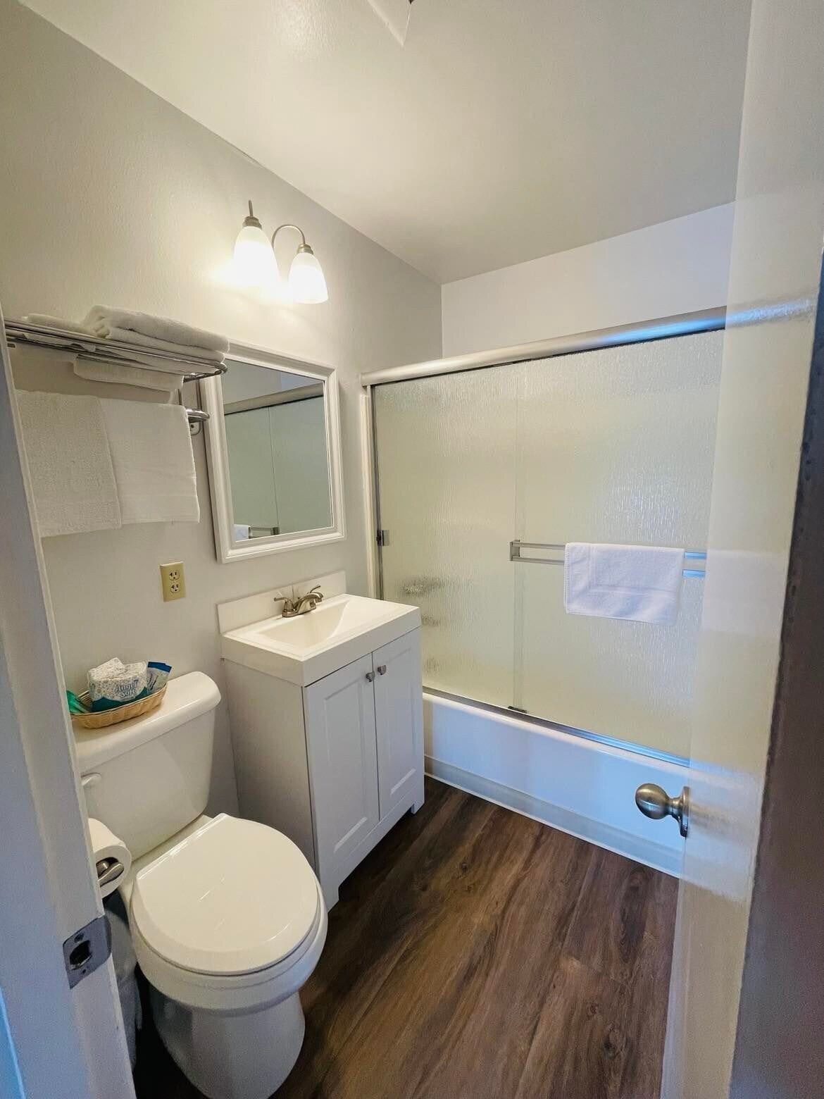 A bathroom with a toilet, sink, mirror, and glass shower enclosure.