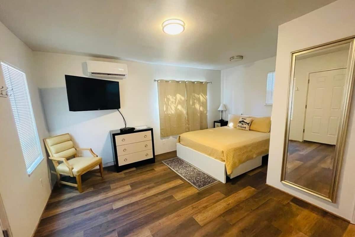 A bedroom with a bed, a chair, a dresser, a TV, and an air conditioning unit.
