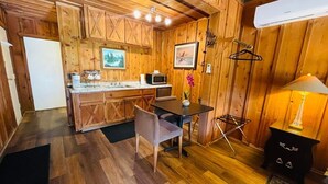 Interior acogedor de una cabaña de madera con cocina, mesa de comedor y una pequeña zona de estar.