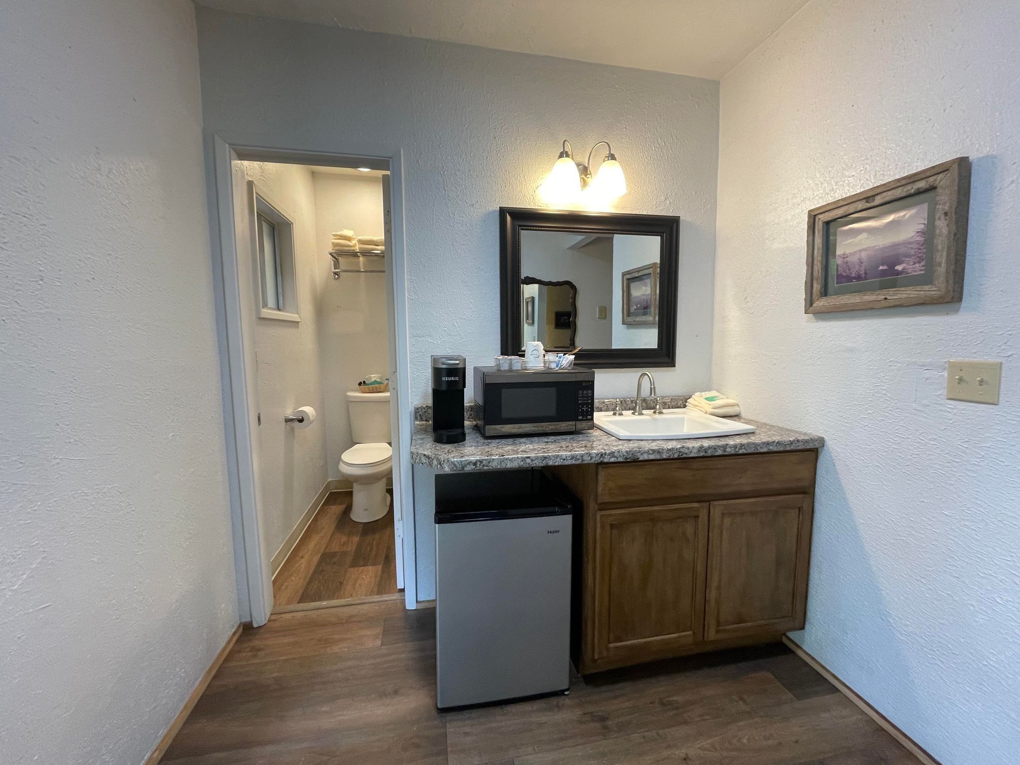 A compact bathroom with a sink, mirror, and a small refrigerator.