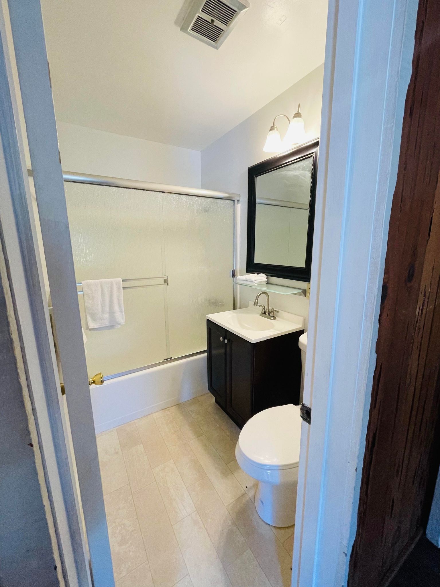 Une salle de bain avec une douche à parois de verre, des toilettes blanches, un lavabo avec un miroir au-dessus et une serviette accrochée au mur.