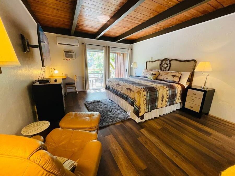 Un dormitorio con techo de madera, una cama con colcha estampada, una mesita de noche con lámpara, un escritorio con lámpara y una silla.