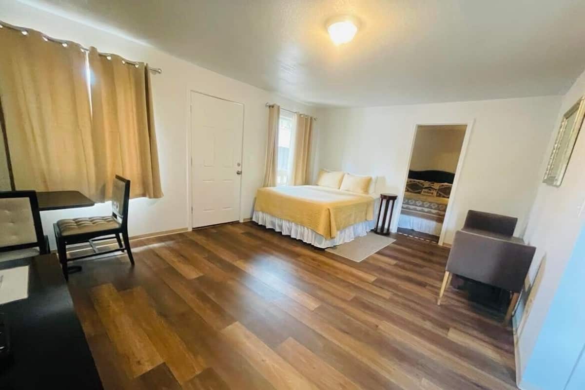 A room with a bed, a desk, and a chair. There is a door and a window with curtains.