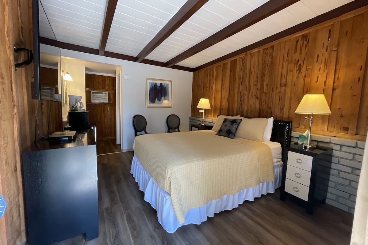 A bedroom with a large bed, wooden walls, a desk, and a chair.