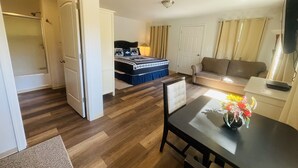 Habitación de hotel con cama, sofá, mesa de comedor y televisión sobre un mueble.