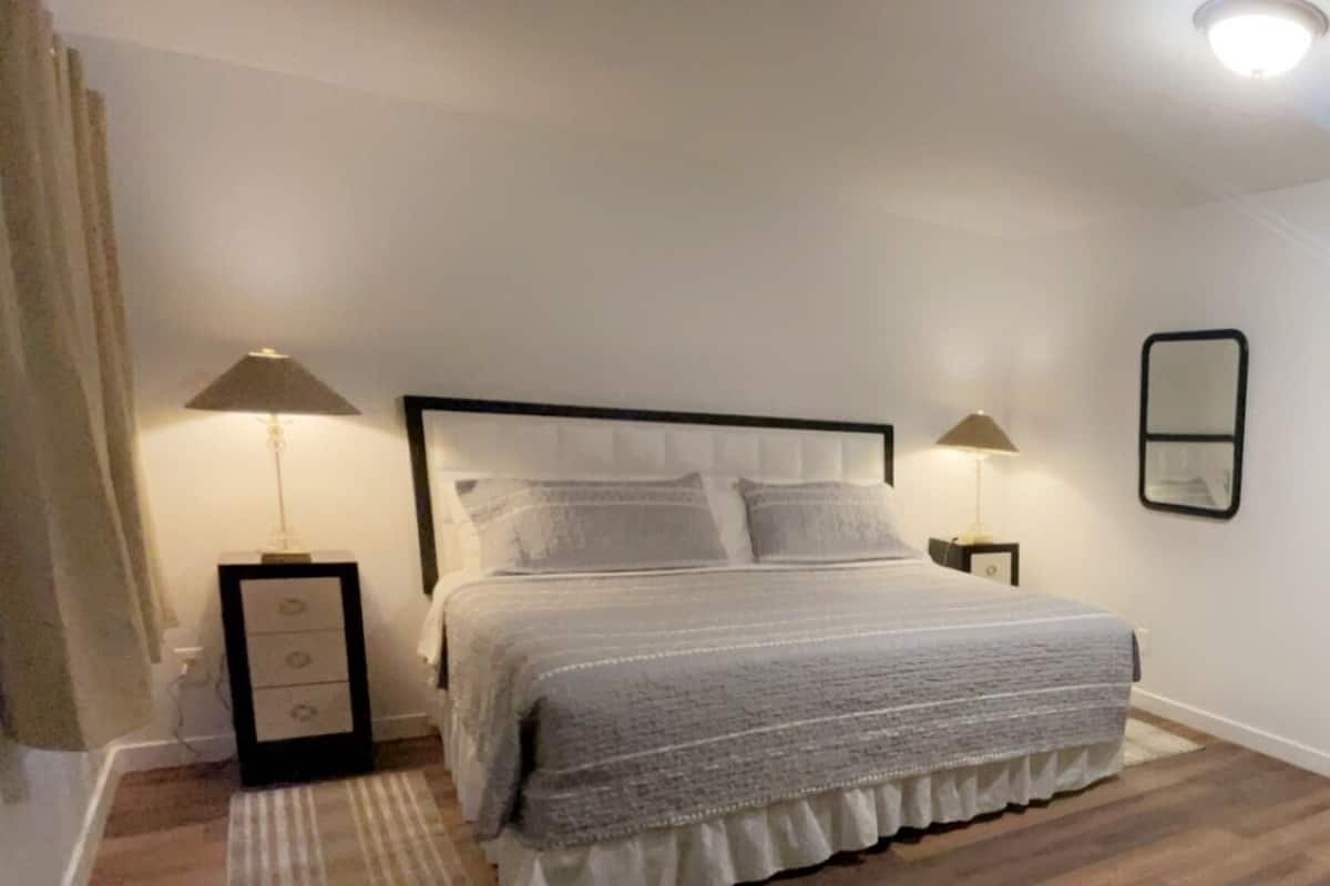 A bedroom with a bed, two bedside tables, a nightstand, a mirror, and a chair.