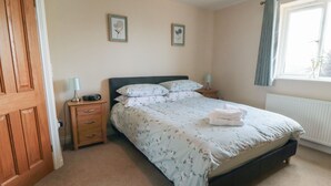 A bedroom with a bed, two bedside tables, a nightstand, a window with curtains, and two wall-mounted pictures. - Cherry Garth (Whitby)