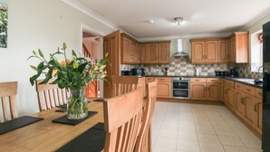 A kitchen with wooden cabinets, a tiled backsplash, and a central island with chairs. - Cherry Garth (Whitby)