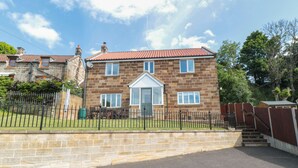 A two-story stone house with a red-tiled roof, a front porch, and a fenced yard. - Cherry Garth (Whitby)