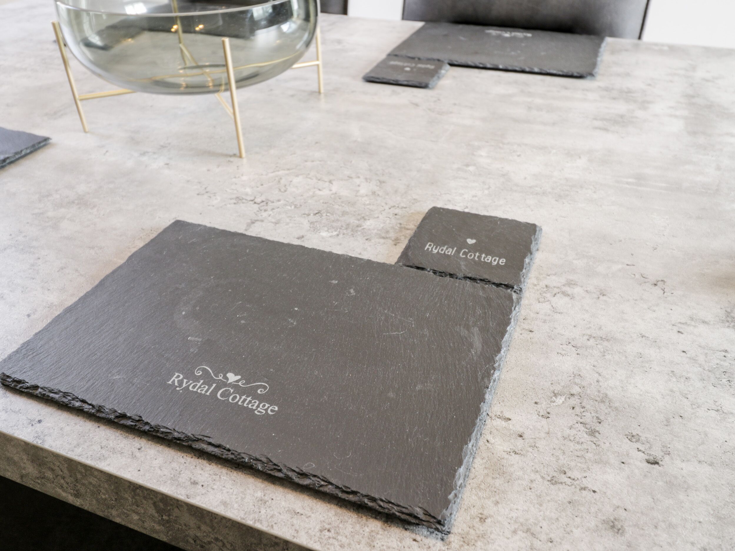 A table with slate placemats labeled "Rydal Cottage" and a glass bowl on a stand.