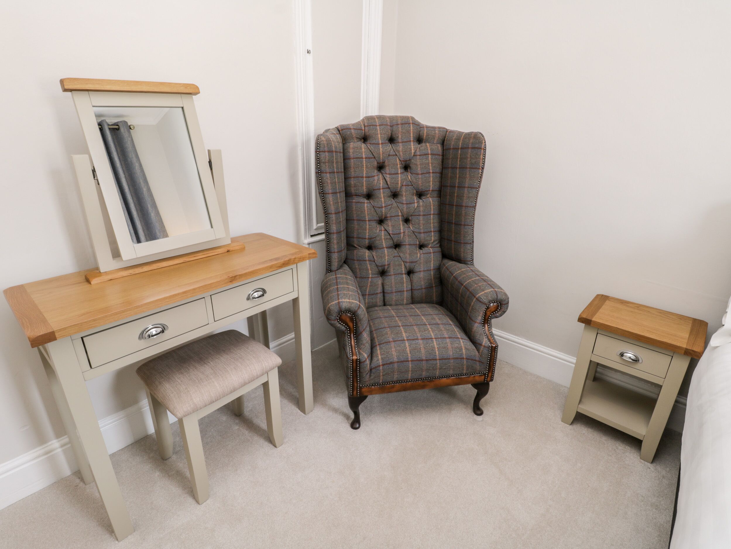 A room with a wooden vanity, a tufted armchair, and a small bedside table.