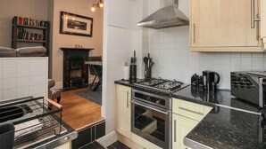 Una cucina compatta con piano cottura a gas, forno e cappa aspirante integrata. Si vede una libreria e un quadro incorniciato appesi al muro.