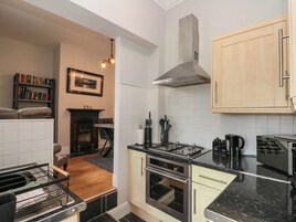 A compact kitchen with a gas stove, oven, and a built-in range hood. There is a bookshelf and a framed picture on the wall.