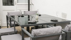 Un'area pranzo esterna moderna con tavolo in vetro e sedie grigie imbottite.