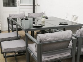 Un'area pranzo esterna moderna con tavolo in vetro e sedie grigie imbottite.
