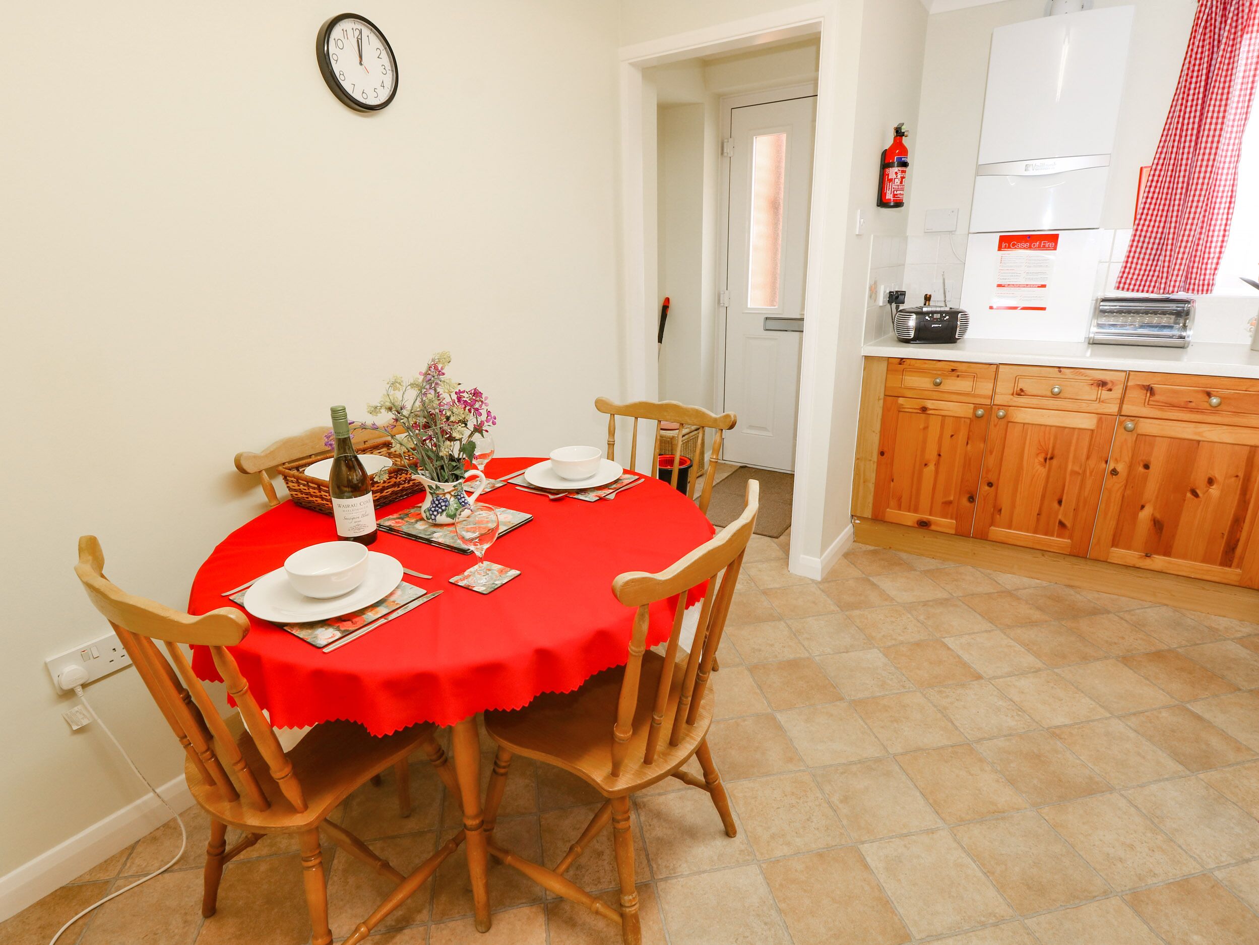 A dining area with a red tablecloth, wooden chairs, and a clock on the wall.