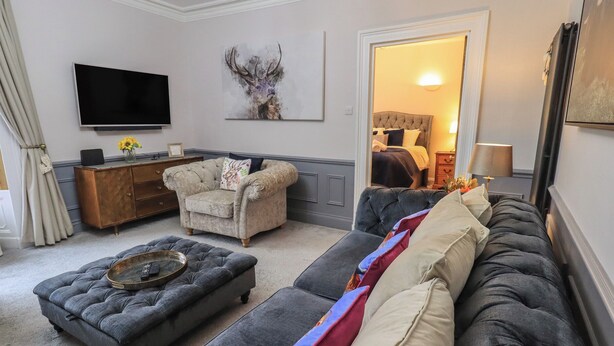 Una sala de estar con un sofá gris, un sillón pequeño, una mesa de centro, un televisor y un mueble.