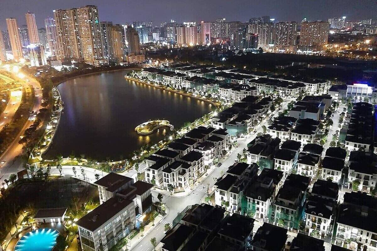 Une vue aérienne nocturne d’une ville, avec une rivière, des immeubles de grande hauteur et un quartier résidentiel caractérisé par des logements uniformes.