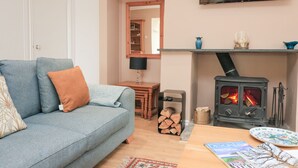 Ein gemütliches Wohnzimmer mit einer Couch, einem Tisch mit Zeitschriften, einem Kamin und einem an der Wand befestigten Fernseher.