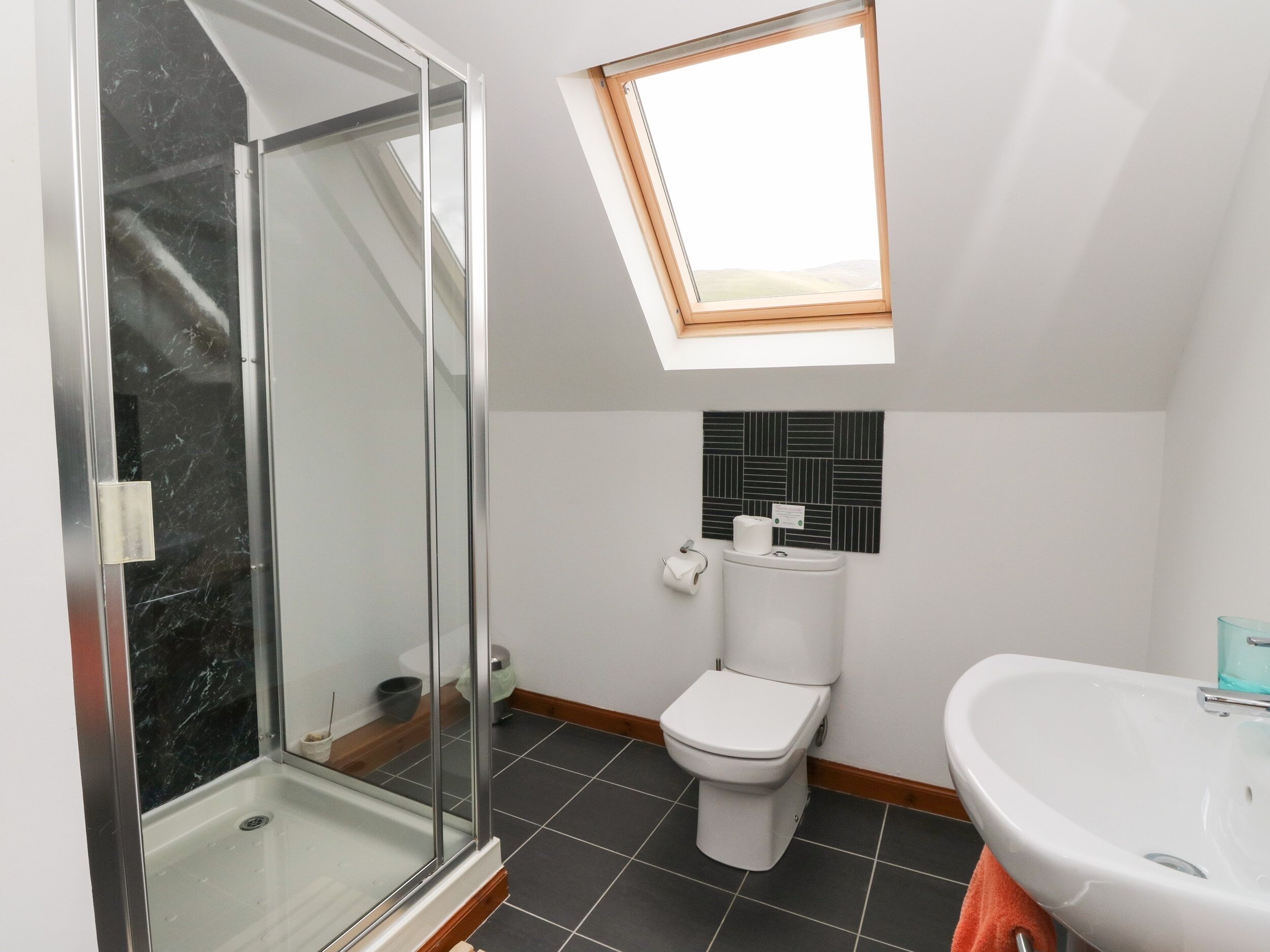 Ein modernes Badezimmer mit Duschkabine aus Glas, einem Oberlicht, einer Toilette und einem Waschbecken.