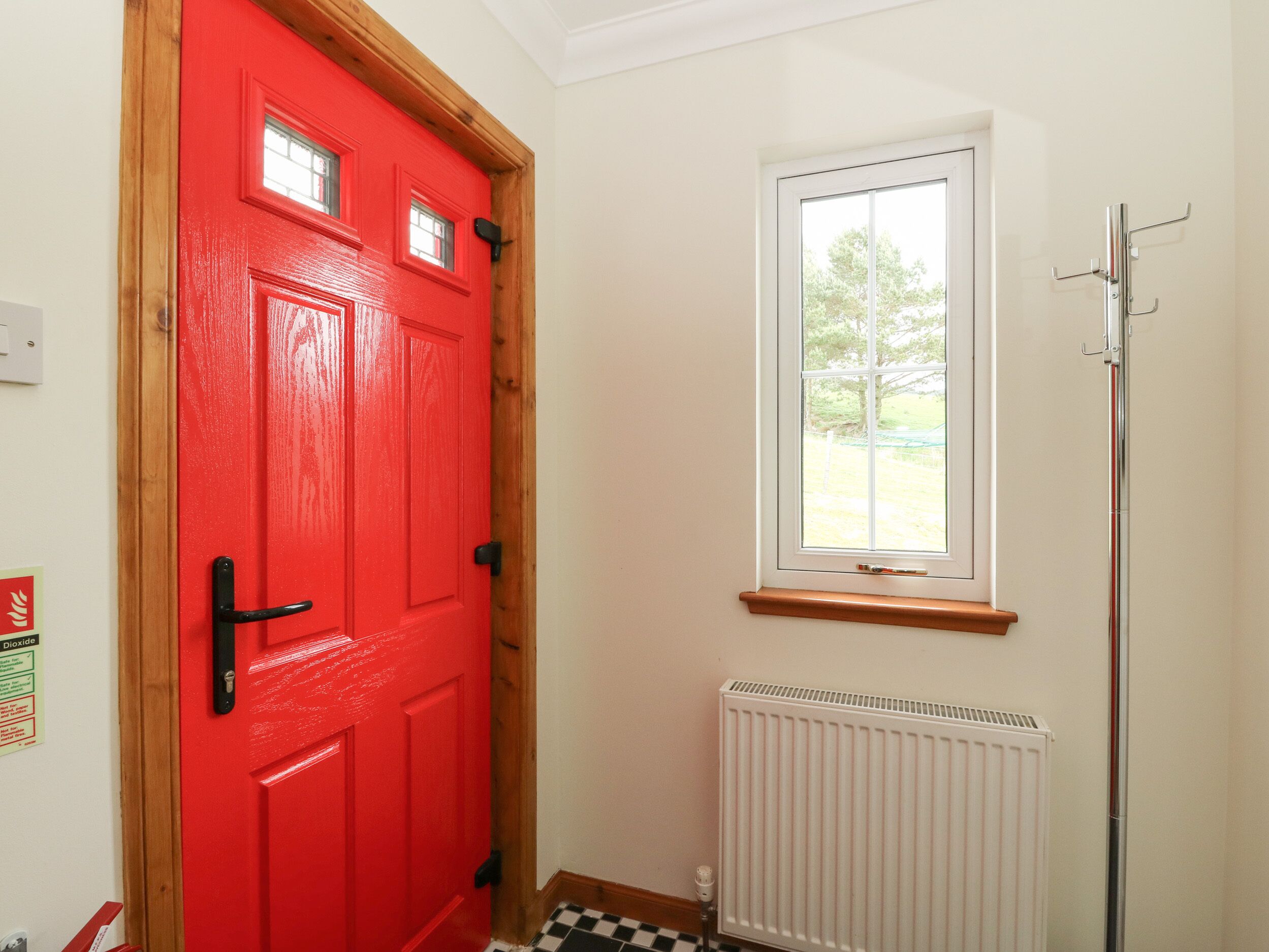 Une porte rouge avec une fenêtre au-dessus, un radiateur et un sol à carreaux noirs et blancs.