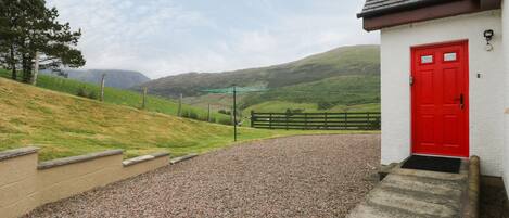 A building with a red door, gravel driveway, and a view of green hills in the background.