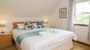 A neatly made bed with a wooden headboard, two bedside lamps, and a window with curtains. - Brae Mhor Cottage (Fort William)