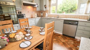 Een keuken met een eettafel gedekt voor thee, een vaatwasser, en een raam met uitzicht op groen.
